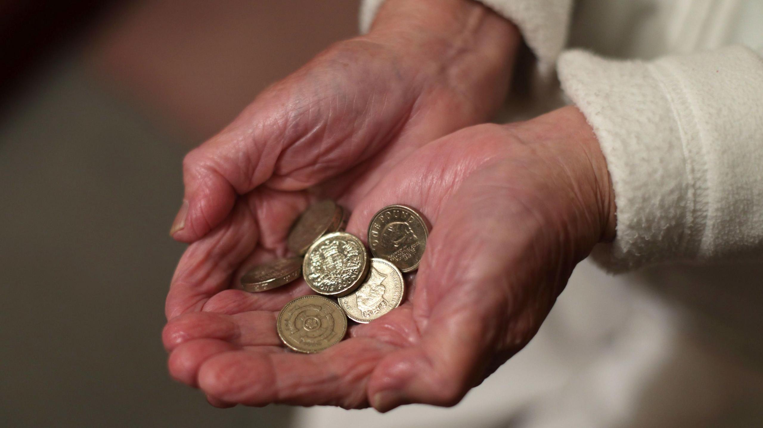 An image showing an elderly lady's cupped hands as she holds six pound coins.