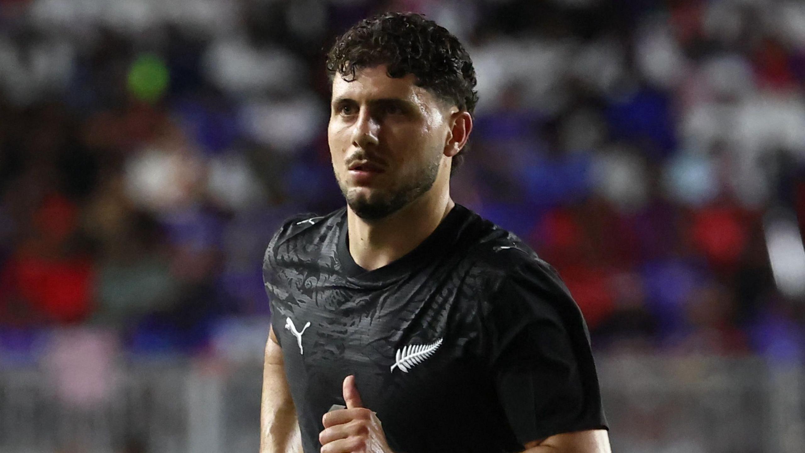 Liberato Cacace wearing New Zealand's black shirt during a game while running along.