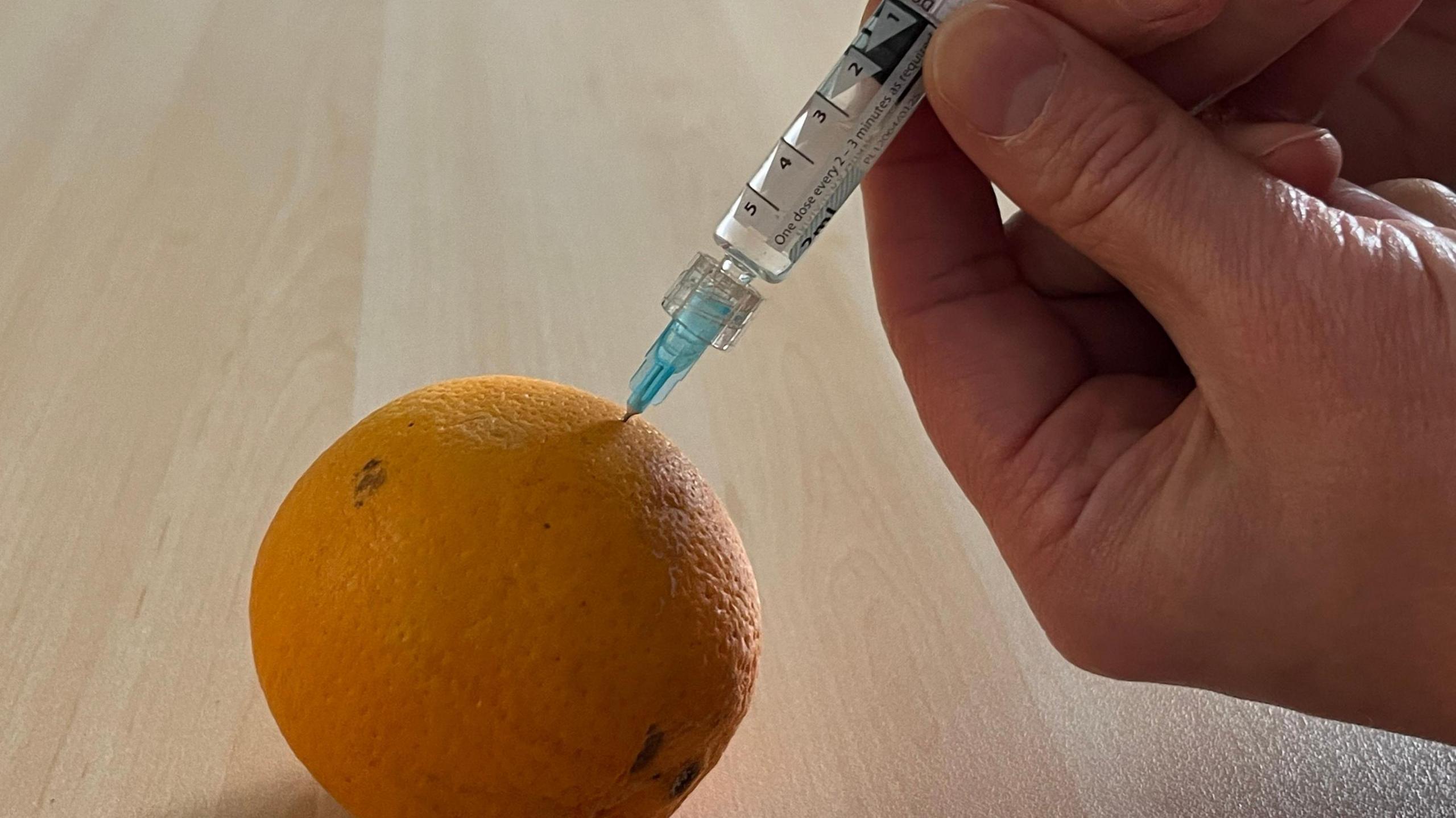 Someone injecting a orange using  syringe