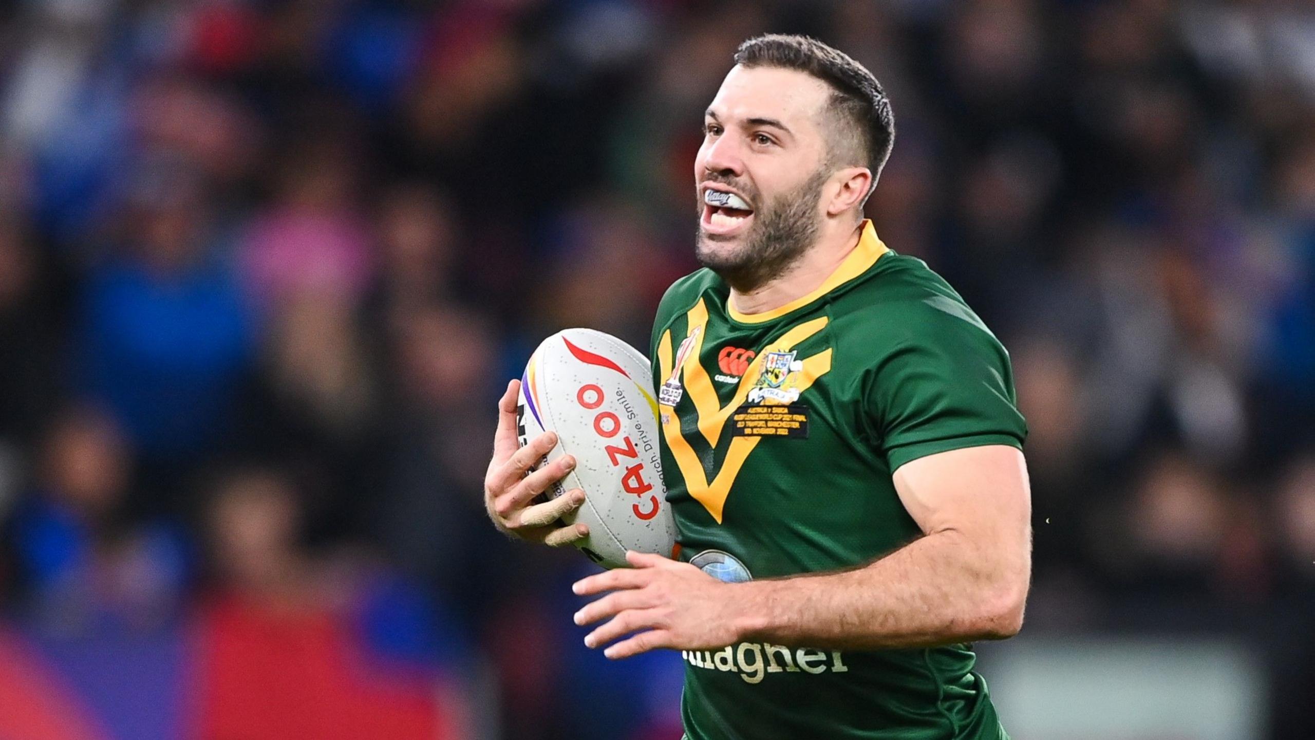 James Tedesco in an Australia jersey running from right to left with the ball, his mouth open to reveal a branded mouthguard