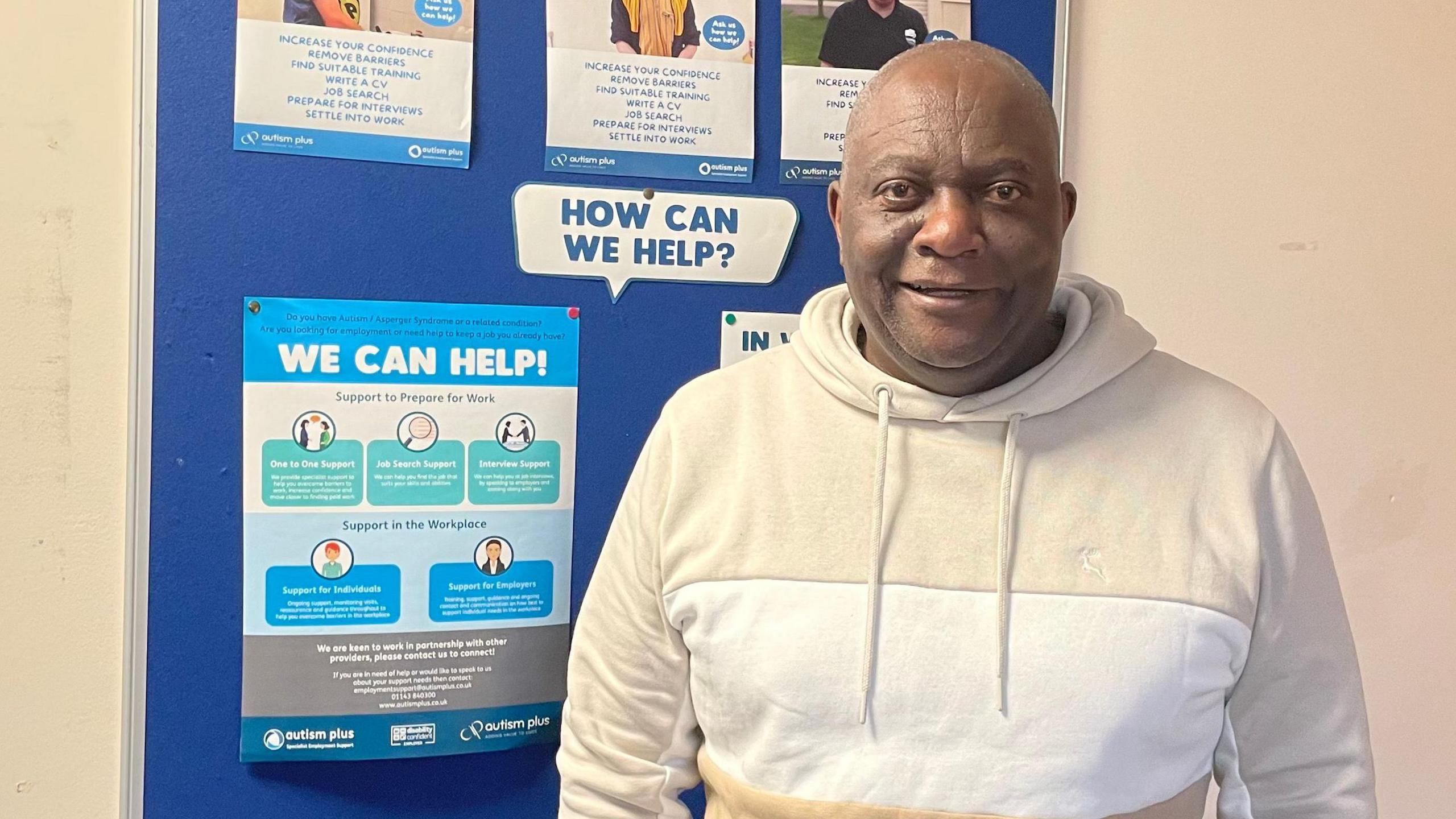 Christopher Nyabezi, stood in front of Autism Plus posters offering help and support with work.