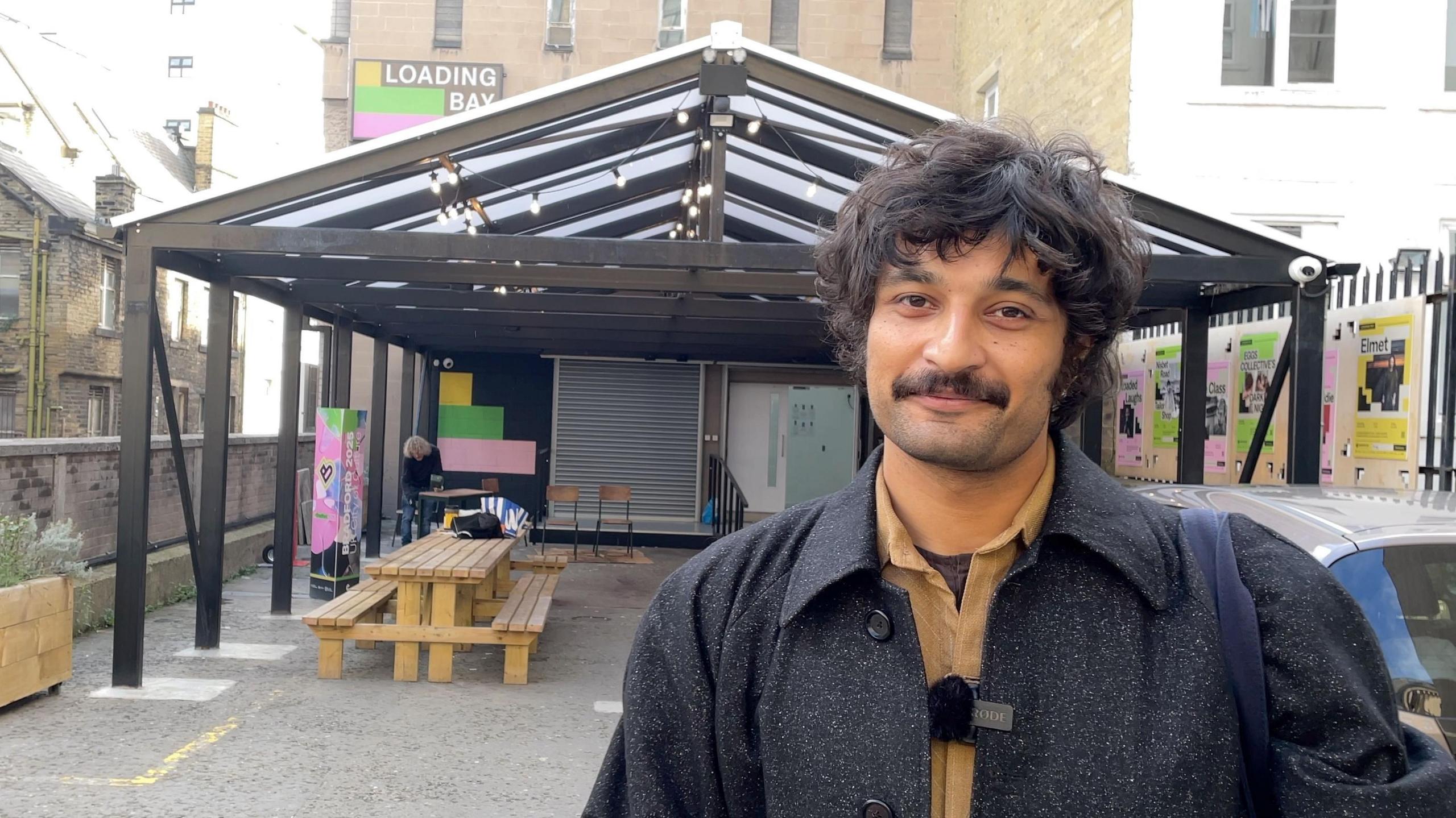 Zain Ali standing outside The Loading Bay wearing a black tailored coat.