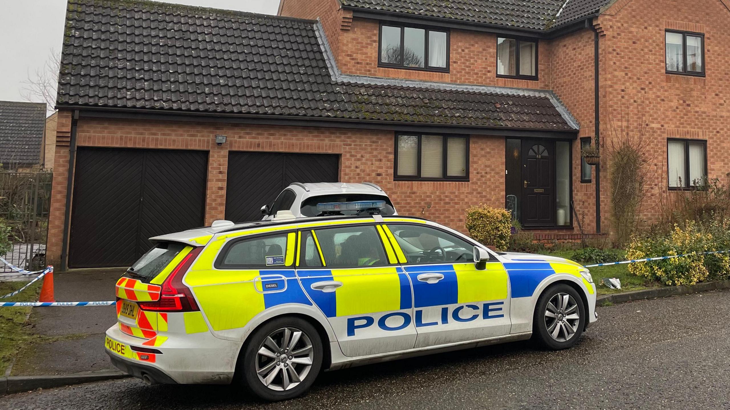 A police car is outside a property in Lingwood Park in Peterborough. Around the house is blue and white tape as a police cordon. 