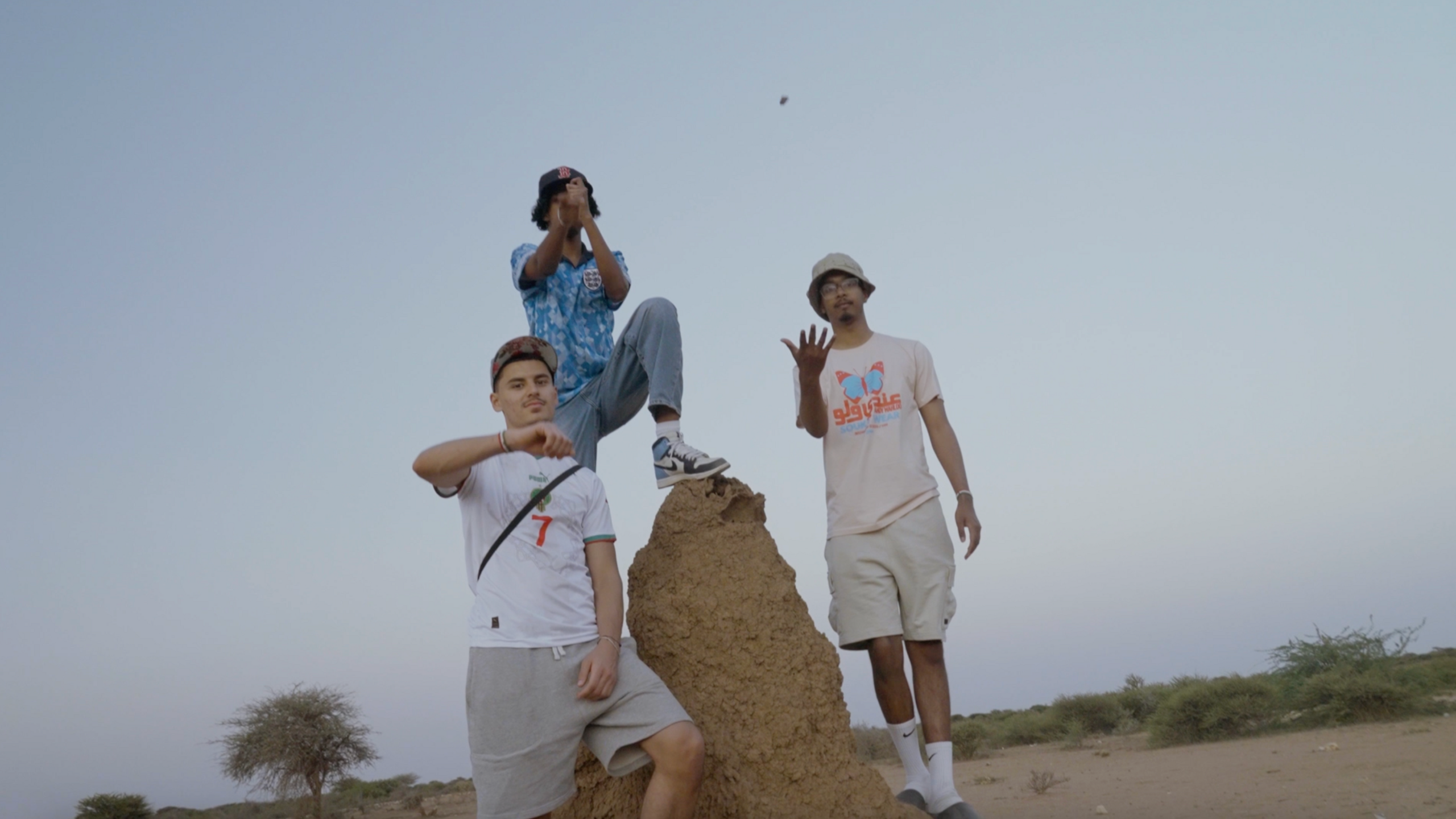 Zak Hajjaj, Abu Finiin, Kayum Miah standing next to a large ant hill with Abu standing on top