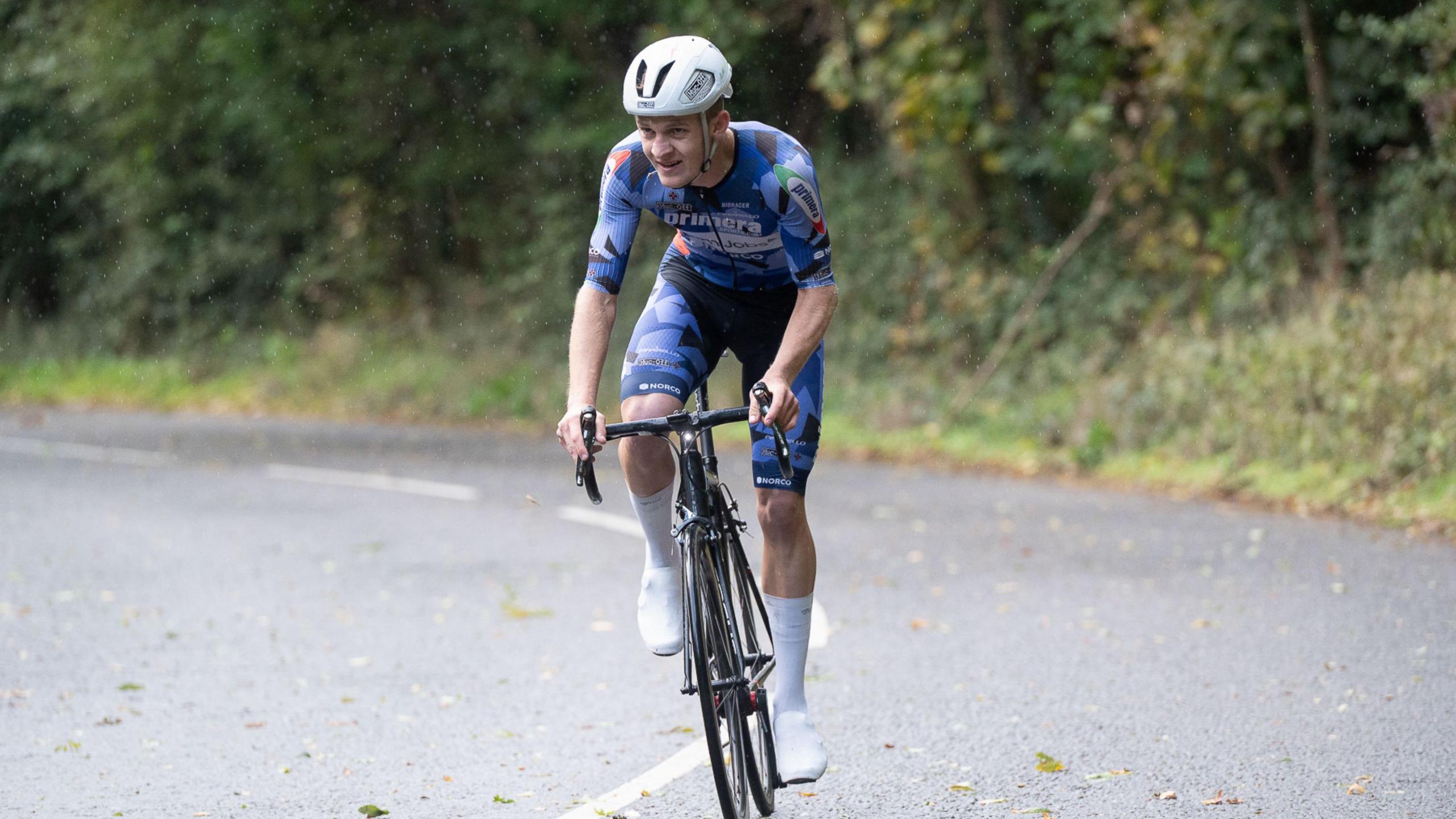A man wearing a white bike helmet and a light blue lycra-style cycling outfit as he pedals up Belmont Hill in North Somerset