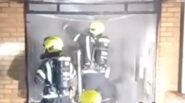 Two firefighters attend to a fire with two brick walls either side of an opening.