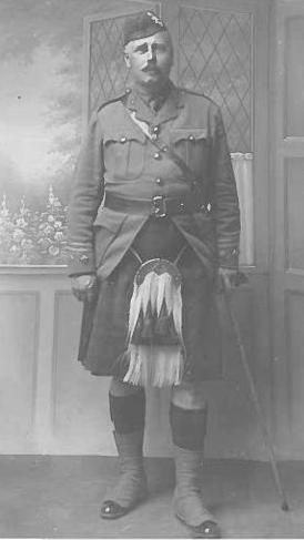 Black and white picture of JD Swanston. He is wearing a uniform including a kilt, large sporran and hat. He has a walking stick and a moustache.