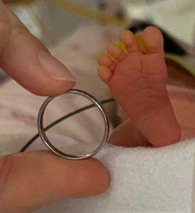 Finger and thumb holding wedding ring next to baby's foot