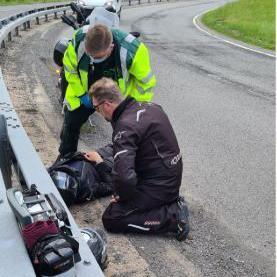 A man is treated on the side of the road with a motorbike in the background