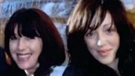 An older and a young woman, both with long dark hair, stand close together smiling.