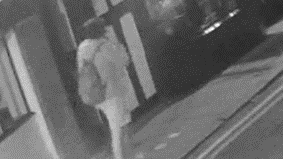 A black and white CCTV image, showing a person walking on a pavement.