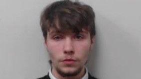 A police mugshot of a teenage boy who has a serious expression. He has brown hair which covers his forehead and eyebrows.