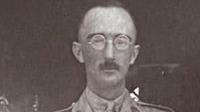 A black and white image of a man with a moustache and round framed glasses.
He is looking straight ahead and not smiling at the camera.