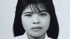 A black and white image of woman with shoulder-length black hair. She is wearing a white dress with a heart brooch. 