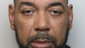 Mugshot of Luke Jones, wearing. a grey jumper with a black top underneath. He has a black beard and is looking into the camera