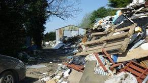 Rubbish including pallets and household waste piled up at the site in Holbeach. A corrugated steel building can be seen in the background.