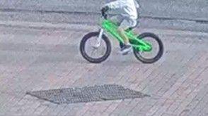 A grainy CCTV image of a boy cycling on a bright green BMX bicycle. His head is out of the frame.