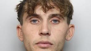 A mugshot of a man who looks directly at the camera. He has brown hair, slightly curly, which covers his forehead.