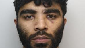 A police mugshot of Hassan Jhangur. He has dark facial hair and dark, slightly curly hair.