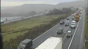 Overhead cctv view of vehicles queuing on a carriageway next to a field in the middle of the M62, with Pennine hills rising in the backdrop.