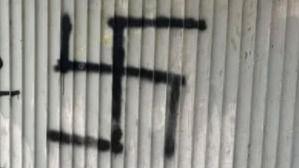 A large black swastika crudely spray painted onto a corrugated wall