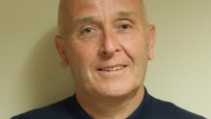 A close-up image of councillor Paul Walker smiling. He is wearing a black jumper and is standing against a light-coloured wall.