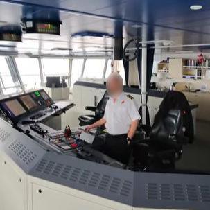 A man in a nautical uniform at the controls of a large ship
