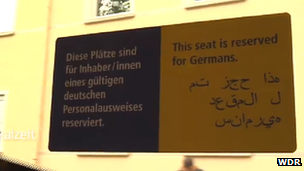 A sign reading "This seat is reserved for Germans" in English, also with German and Arabic text