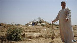 A Bedouin man holds an olive tree root near a destroyed building in al-Arakib