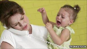 Mother on phone and holding crying girl