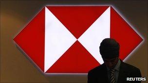 A worker is silhouetted against an illuminated sign in a branch of HSBC in the City of London