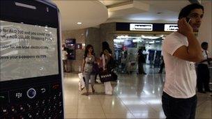 A man speaks on his mobile phone as he stands next to a display of a BlackBerry at a shopping mall in Dubai