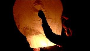 A woman holds a sky lantern as it is being launched