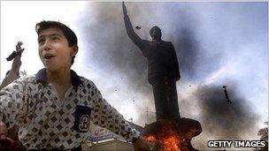 A boy cheers in front of a statue of Saddam Hussein that was set on fire on 12 April 2010