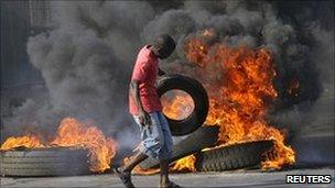 A demonstrator throws a tyre on a burning barricade during riots in Maputo