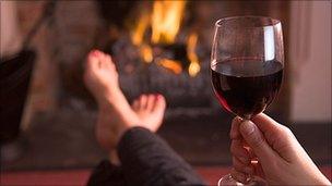 Person drinking wine with feet up in front of fire