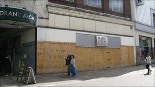 People walking past a boarded up shop