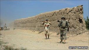 Afghan civilians bare cheir chests to show they are unarmed to a US Soldier