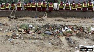 Municipal Corporation of Delhi workers sit on a pavement outside the Commonwealth Games village