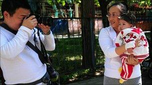 A father takes a photograph of his baby girl being held in her mother's arms at a park in Beijing