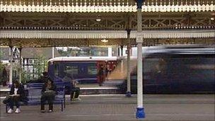 Passengers on a train platform as a train drives past