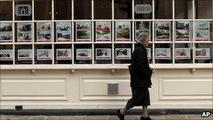 Woman walks past estate agent's window