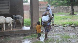 Woman wades through muddy fields with her children