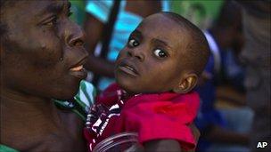 A woman carries a child with symptoms of cholera at the entrance of the St. Catherine hospital in the Cite Soleil neighbourhood in Port-au-Prince, Haiti,Thursday, Nov. 11, 2010