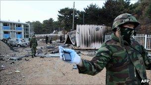 A South Korean soldier prevents photographers from approaching the ruins of a bombed-out military residence area on Yeonpyeong island