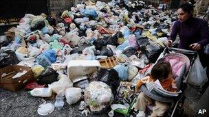 A woman pushing a baby stroller makes her way through uncollected rubbish in Naples, Italy, 22 November 2010