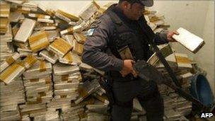 A policeman holds one of hundreds of marijuana packs found inside a house in the Alemao complex