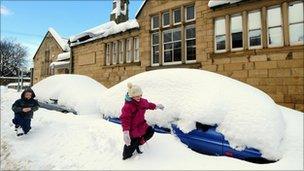 Children play next to a row of cars covered in snow in Alnwick, Northumberland, as heavy snowfall continues across the North East