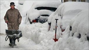 A man tries to clear snow around cars