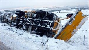 A snow plough delivering grit in the Scottish Highlands slips and overturns